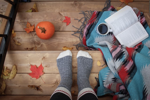 Autumn leaves on steps, woolly socks, a pumpkin, a book and coffee.